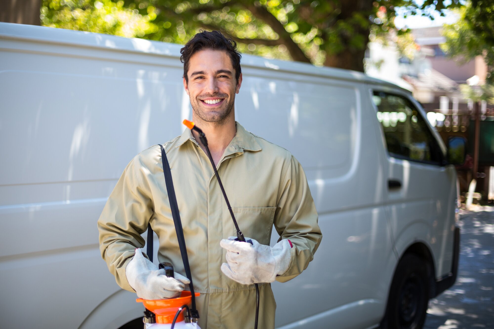 Smiling worker with pesticide sprayer and van on the back